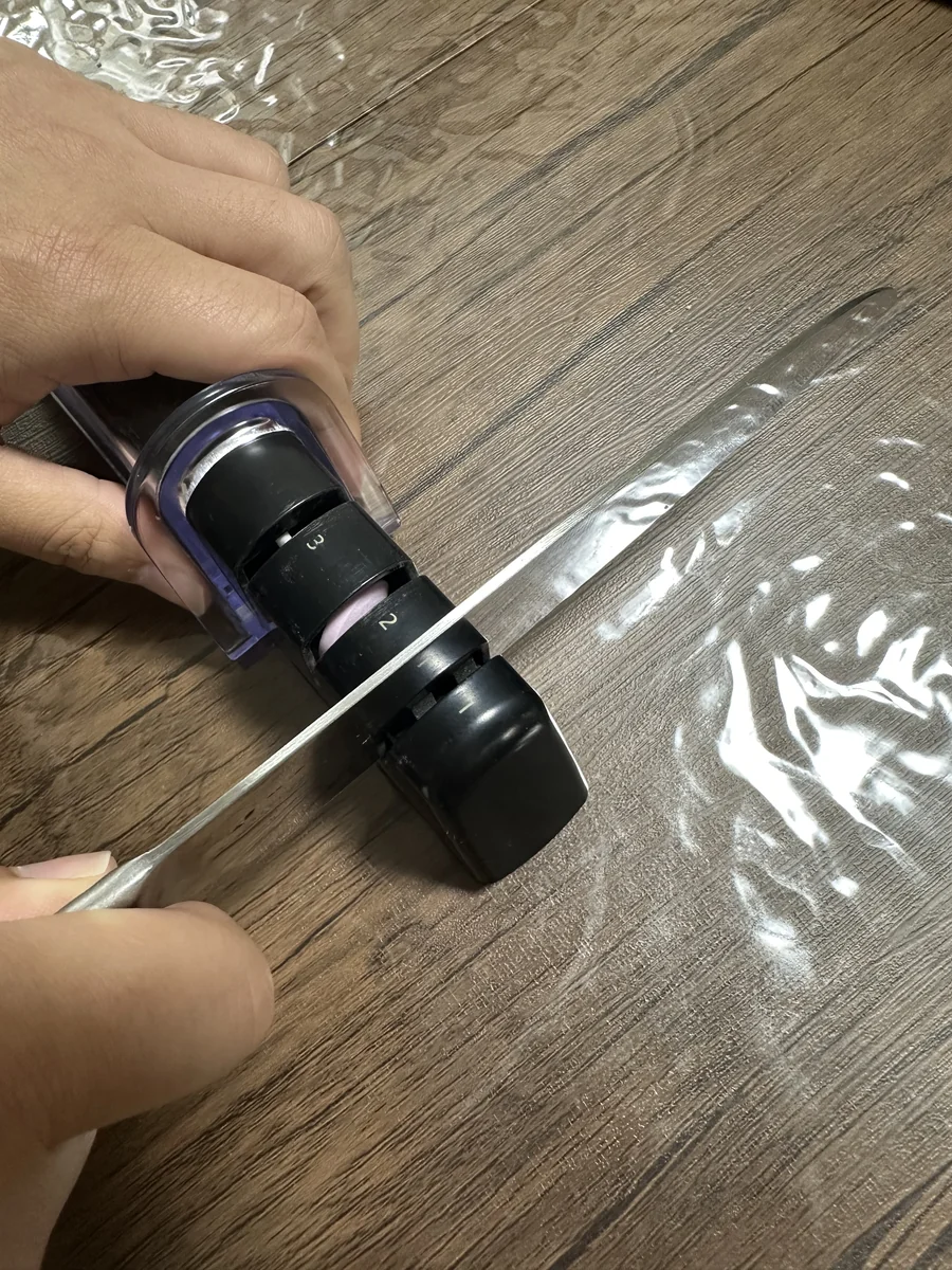 AP-0308 を片手で押さえ、もう片手で関孫六 三徳包丁を溝に入れて引いてるメンテナンス中の手元